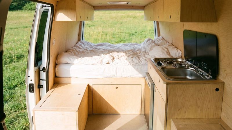Blick durch die offene Hecktür in einen ausgebauten Kastenwagen aus hellem Birkenholz mit Bett